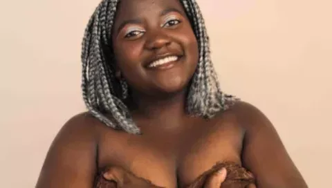 A young woman smiles at the camera as she cups her chest in her hands | CoppaFeel! | breast cancer awareness charity
