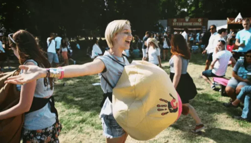 a young woman wanders happily round a festival with a large inflatable breast strapped to her chest