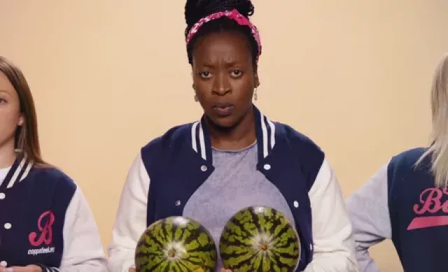 A black woman holding two watermelons close to her chest and looking concerned and confused