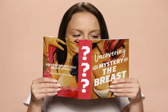 A woman reading a book titled 'uncovering the mystery of the breast' | CoppaFeel! | Breast cancer info and advice
