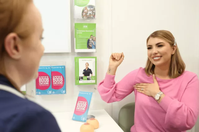 A young woman feeling her chest whilst talking to a healthcare professional | CoppaFeel! | Breast cancer info and advice