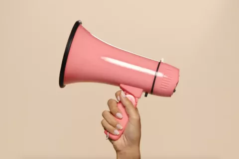 A pink megaphone being held up by a hand