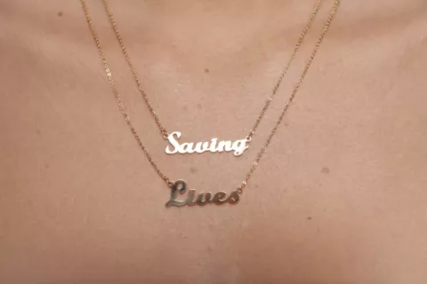 a close up of a gold necklace that reads 'saving lives' on someone's chest