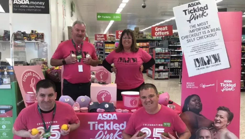 A group of four asda employees dressed in tickled pink t-shirts smiling with a tickled pink awareness stand in their asda store