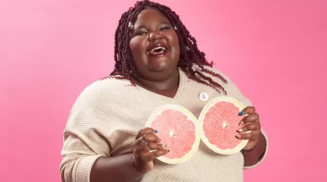 A black woman holding up two grapefruit cutouts up to her chest from Avon's #NormalForMe Campaign