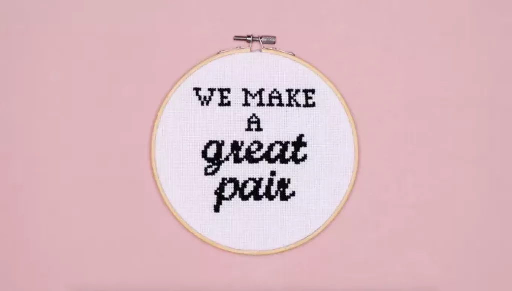 A cross stitch hoop with the wording 'We make a great pair' stitched onto white fabric on a pink background | CoppaFeel!