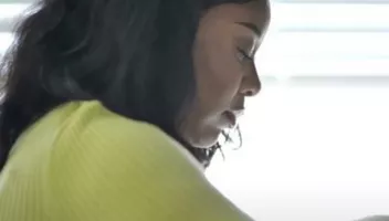 A close up picture of a black woman standing side on wearing a lime green cardigan. The woman picture is called Lucy. CoppaFeel!