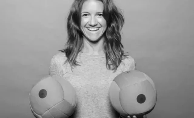 A woman holding up two soft balls shaped like boobs up to her chest