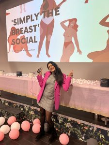 A picture of a woman stood in front of a digital presentation screen, surrounded by pink balloons 