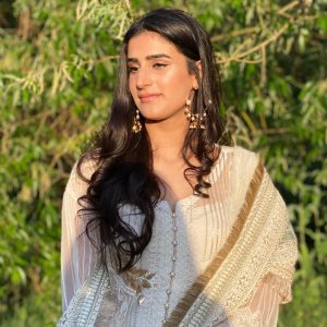 A woman pictured wearing a white and gold sari, stood in her garden