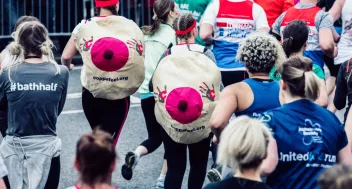 Two people in a crowd running during a marathon with boob suits strapped to their backs
