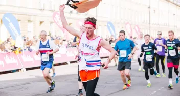 A man running during a challenge event for CoppaFeel!. He is also holding a boob suit
