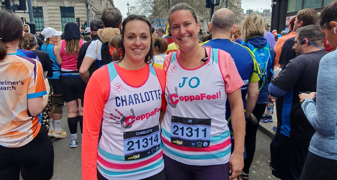Two women stood wearing CoppaFeel! branded running vests smiling with their arms around each other after completing the London Landmarks Half Marathon