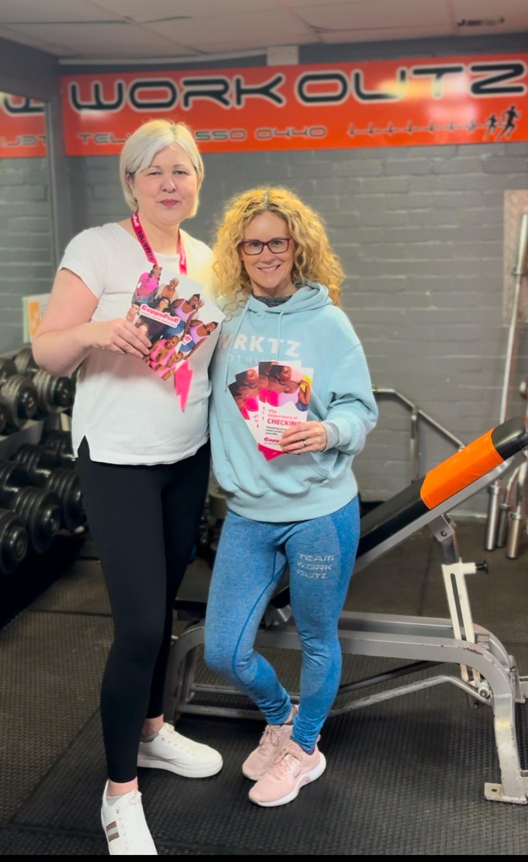 Two volunteers stood in a gym holding CoppaFeel! leaflets