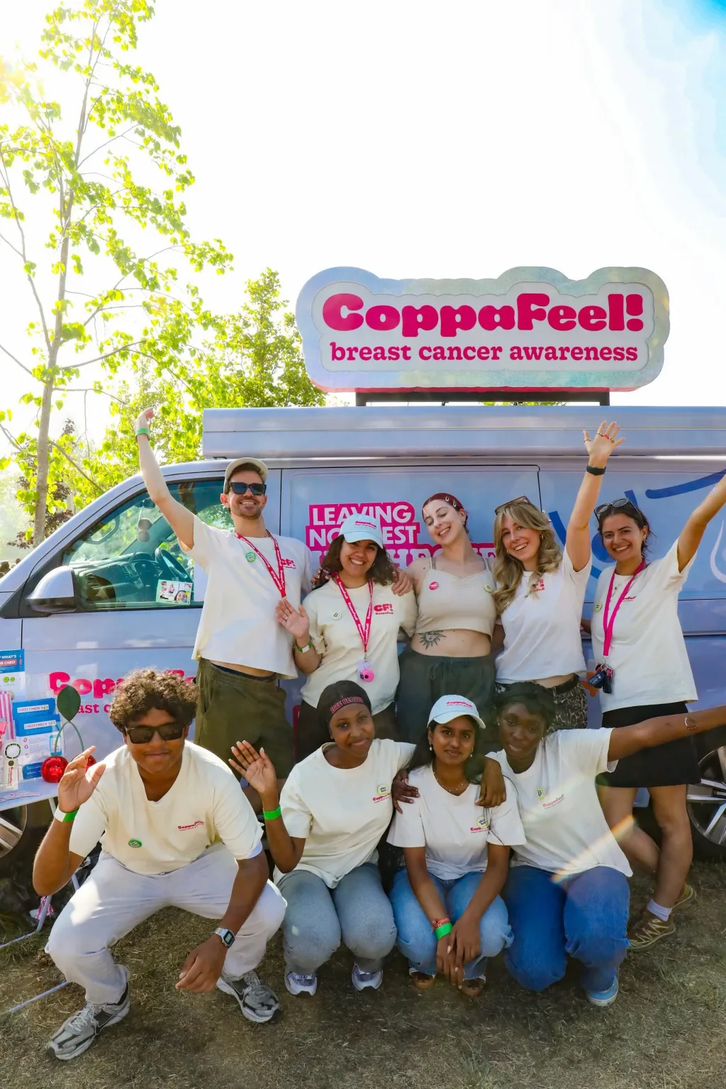 9 people pose in front of the CoppaFeel mobile, wearing CoppaFeel merch